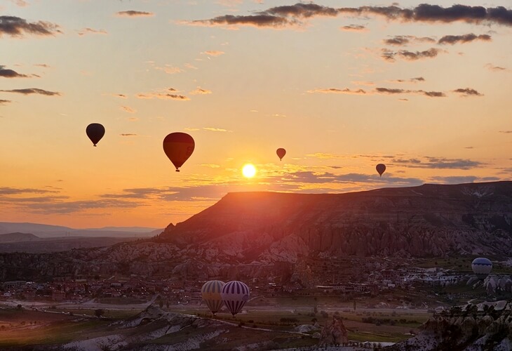 Kapadokya Aşk Vadisi’nde gün batımı manzarası, sıcak hava balonları ve siluet halindeki dağlar eşliğinde